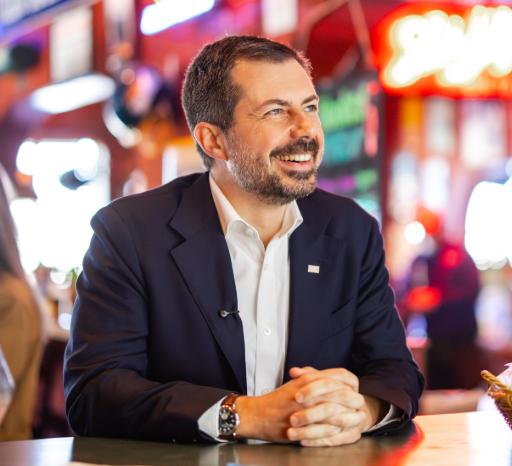 Pete Buttigieg smiles as he sits at a table.